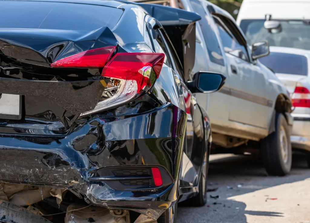 A black car with a heavily damaged rear end is parked beside another vehicle, showing visible signs of a collision.