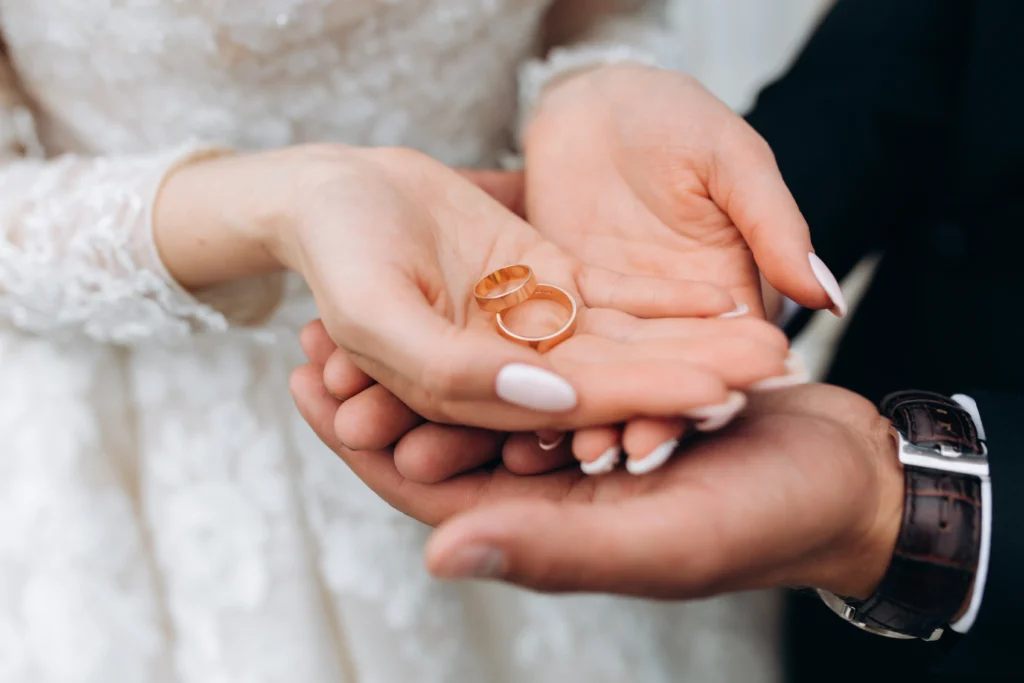A pair of hands gently holding gold rings, adorned with delicate details, showcasing a beautiful bridal look.